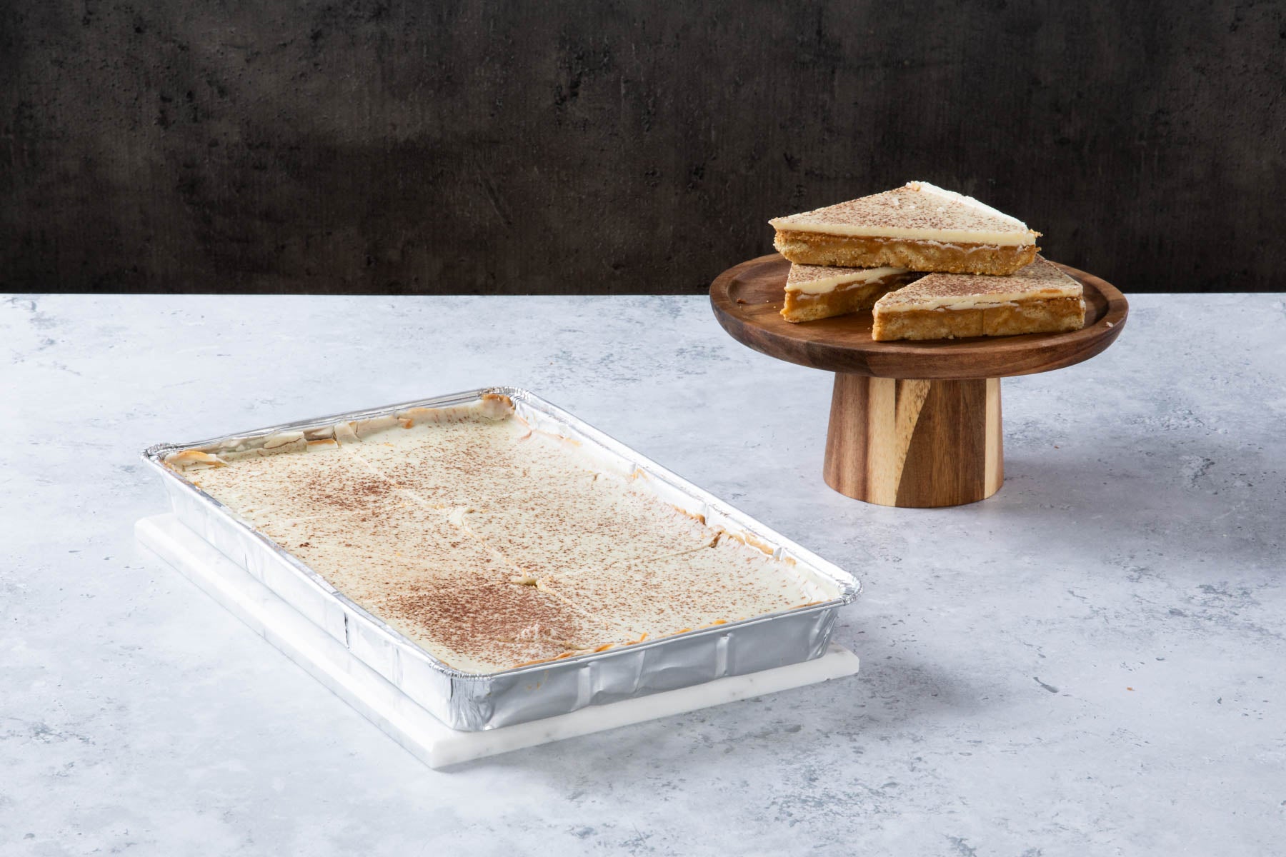 LHMC004-243-1.jpg Caramel shortbread slices with a creamy topping on a wooden stand.