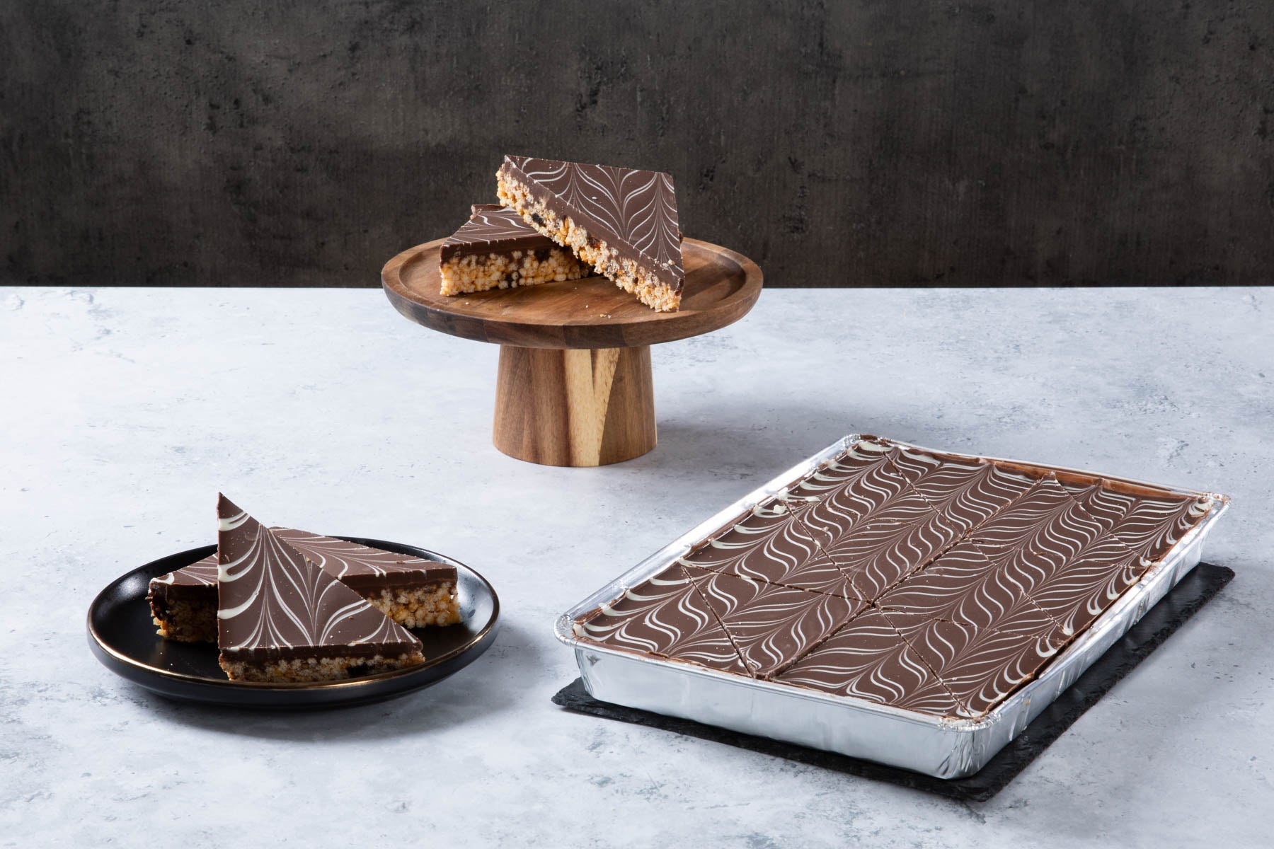 LHMC004-273.jpg Chocolate crispy cake slices with marbled chocolate topping on a wooden stand.