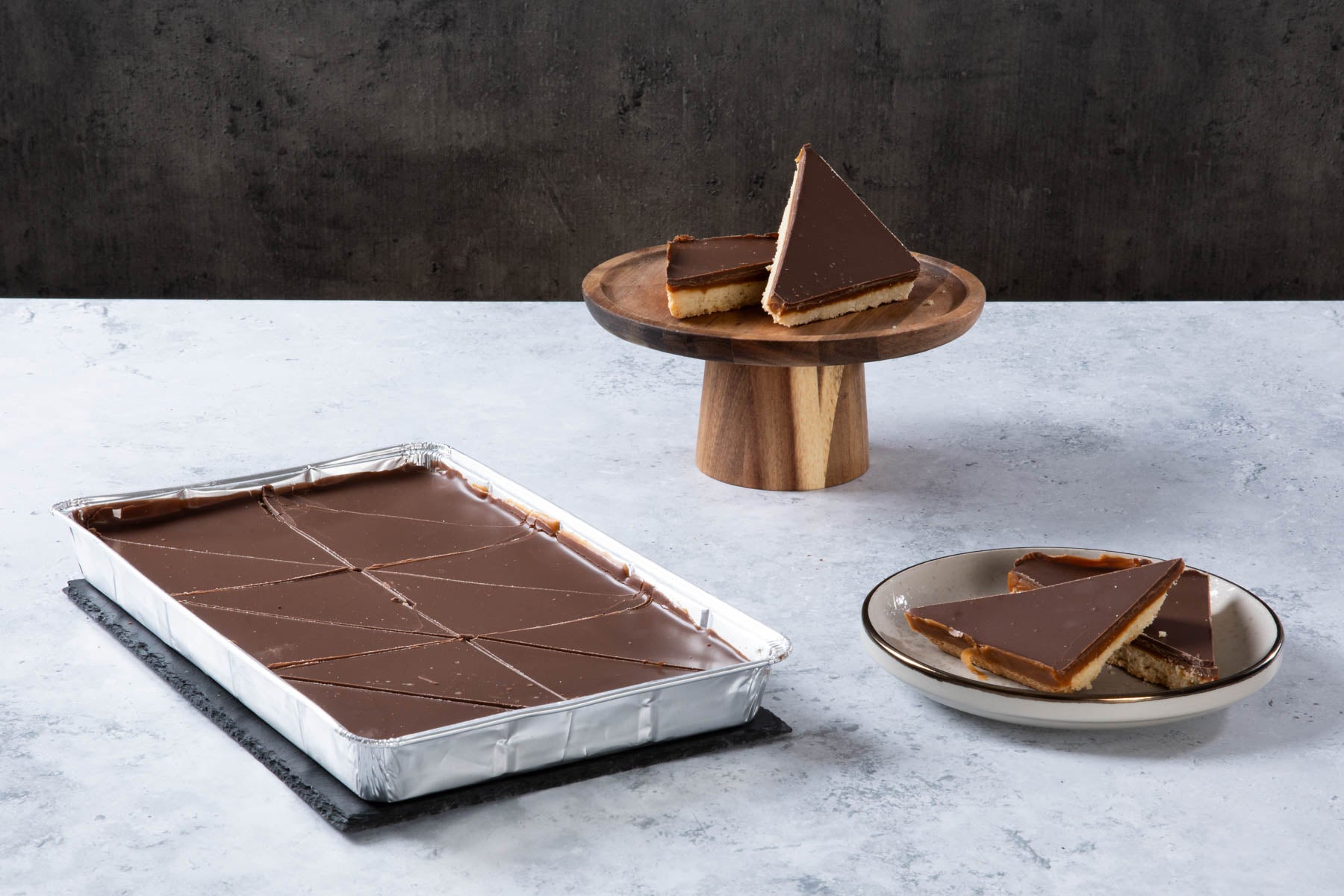 LHMC004-297.jpg Chocolate caramel shortbread slices with a chocolate topping on a cake stand and plate.